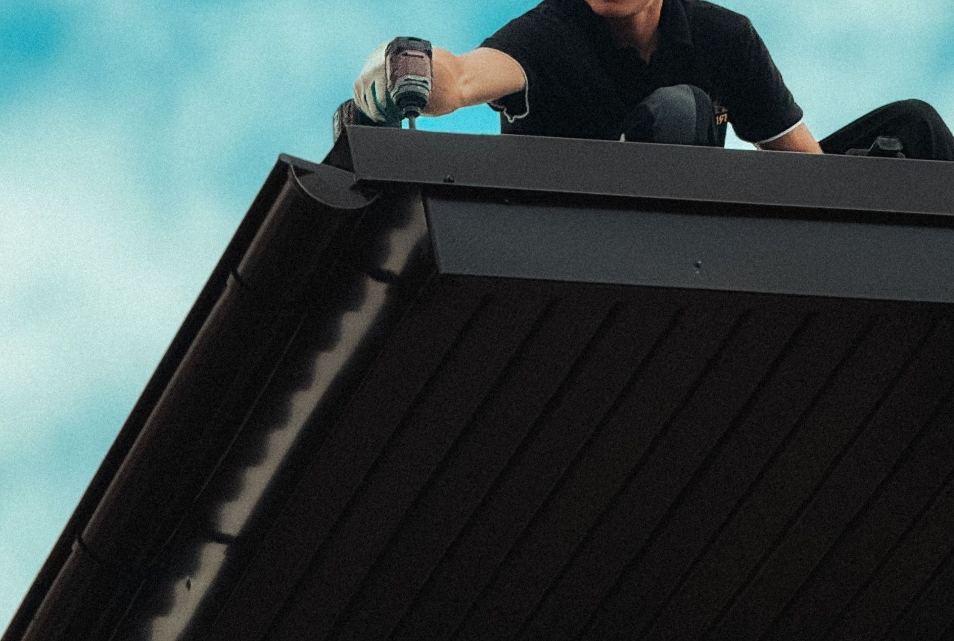 Roofer working diligently on a house roof under a bright blue sky. Professional roofing maintenance in progress.